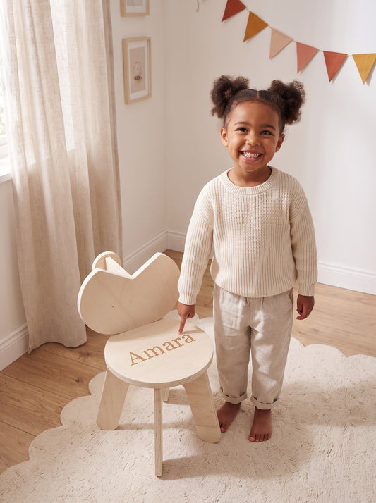 Meisje wijst trots naar haar eigen naam Amara, gegraveerd in de zitting van een houten kinderstoeltje van Studio Verdi